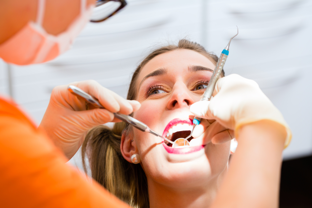 Person sitting while a dentist puts dental tools in their mouth